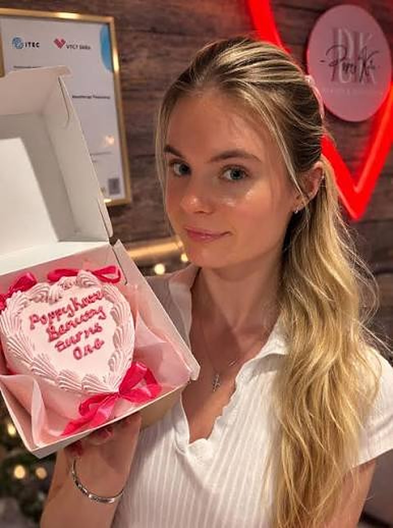 Poppy, founder of Poppy Kate Beauty, smiling and holding a pink heart-shaped celebration cake